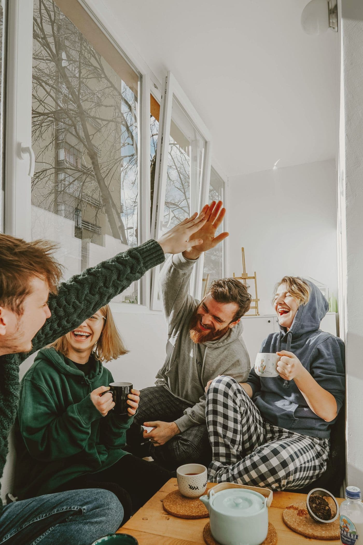 Four friends laughing and high-fiving over coffee