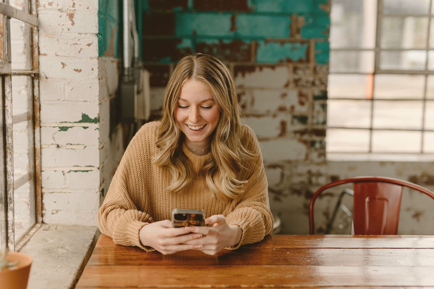 Someone smiling at their phone at a wooden cafe table