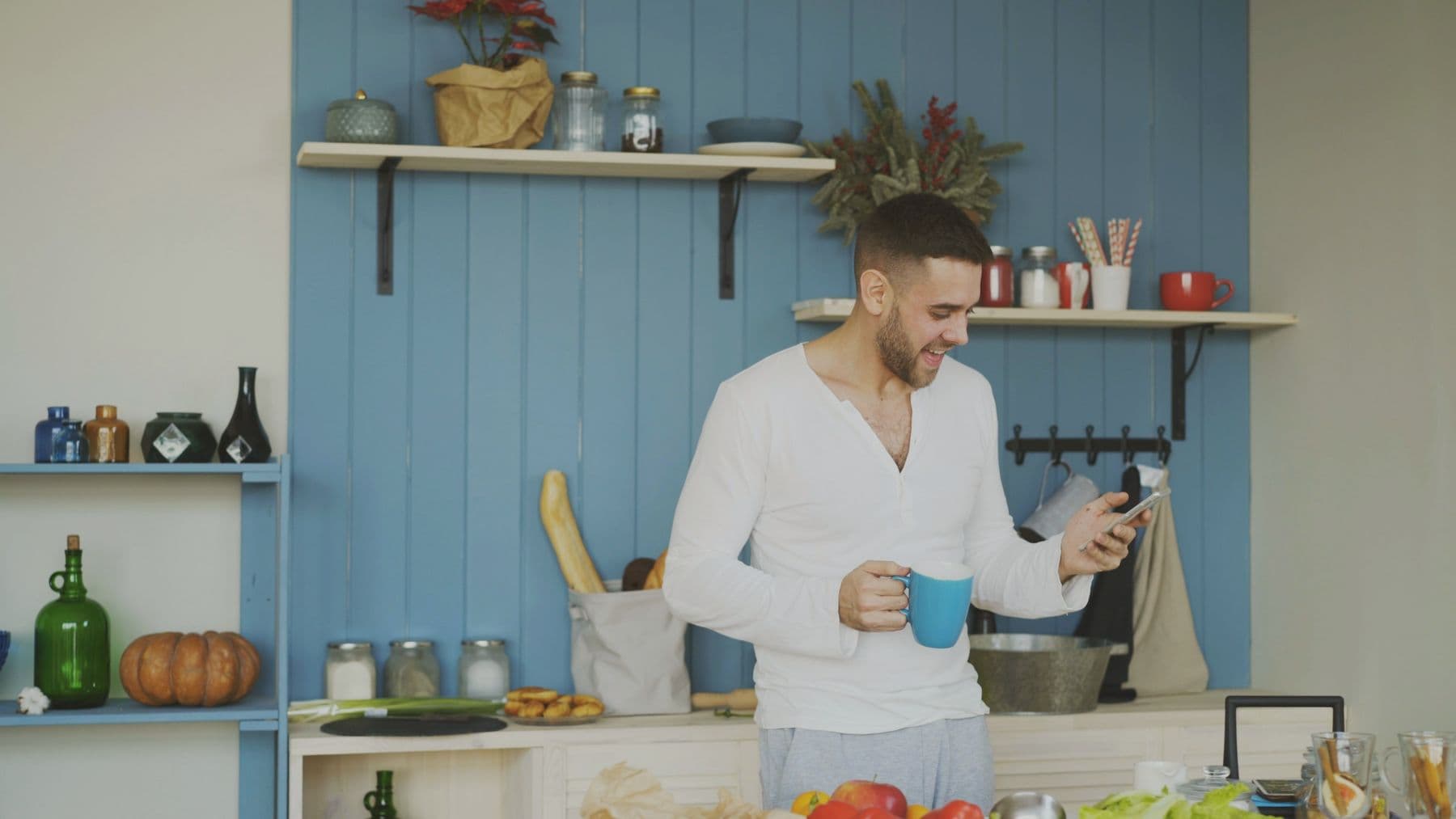 Someone holding a mug and glancing at their phone in a kitchen