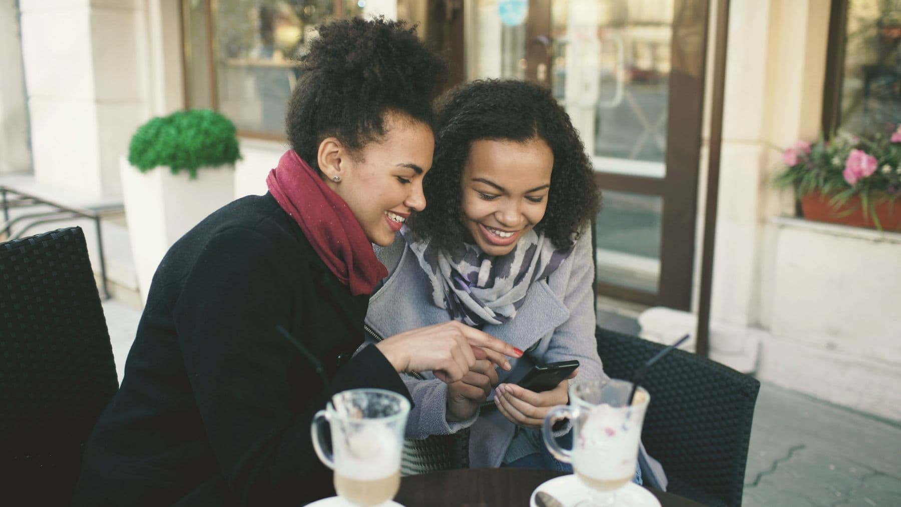 Two friends at a cafe table looking at one phone together