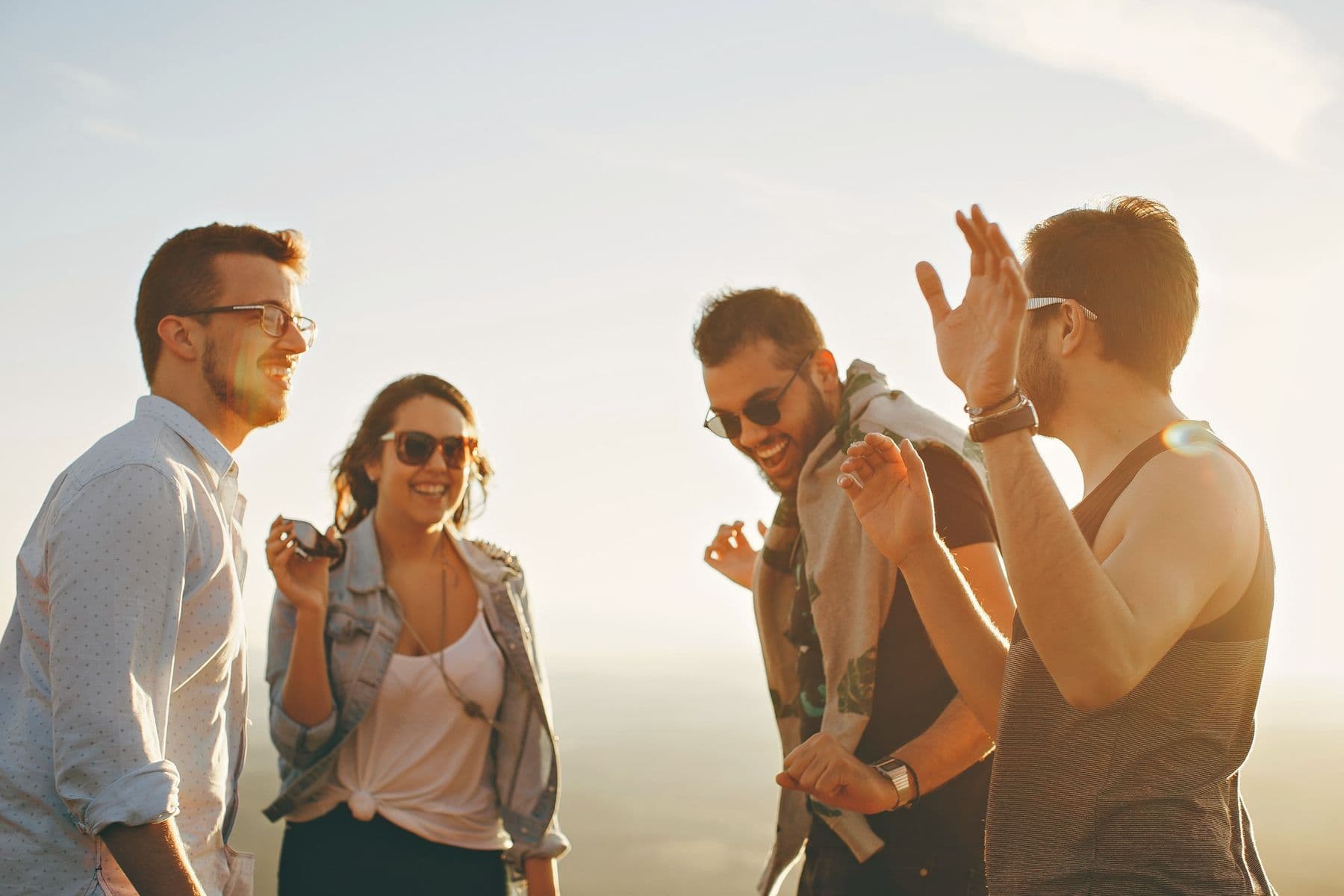 Four friends laughing together outdoors at golden hour